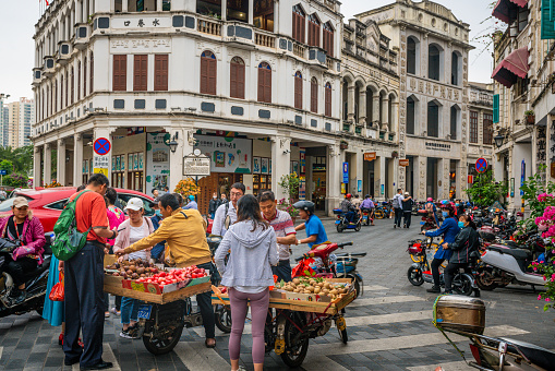 Haikou China , 21 March 2021 : Tourists buying fruits at street food stall in Water-alley street with old colonial buildings and people in Haikou old town Hainan China