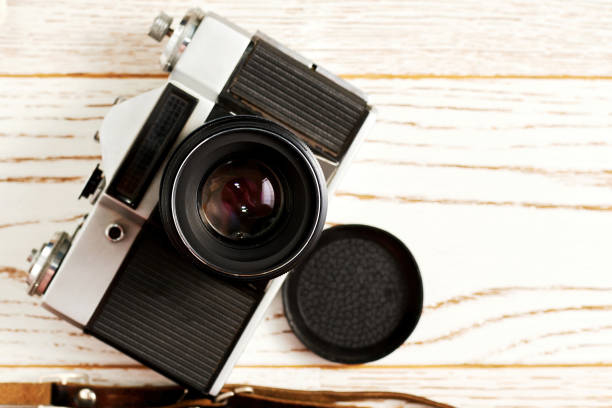 istock Vintage photo camera with opened lens on the wooden surface. Flat lay backdrop template of famous film camera 1311265295