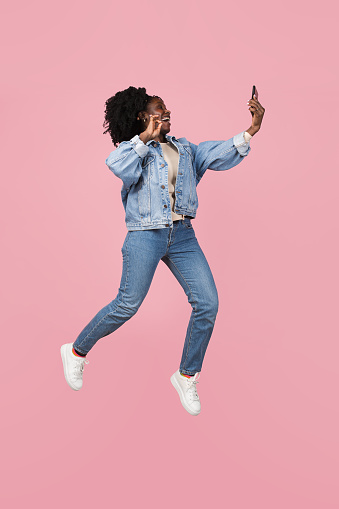 Jumping. African-american beautiful woman's portrait isolated on pink studio background with copyspace. Stylish female model. Concept of human emotions, facial expression, sales, ad, fashion, youth.