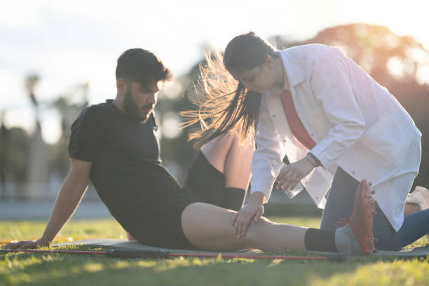 Young footballer is making physiotherapy session with young female doctor. Physiotherapist is touching young man's leg. She is examining carrefuly. sports medicine stock pictures, royalty-free photos & images