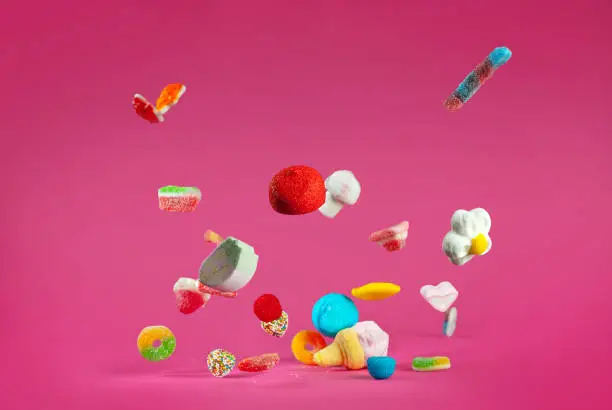 Many colorful candies fall on a pink background. Sweets close up. The concept of childhood and holidays. Copy space and free space for text near sweets.