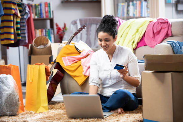 photo d’une jeune femme payant la facture, faisant des achats en ligne utilisant le crédit avec l’ordinateur portatif à la maison, elle est assise sur le sol sur le tapis à la maison :- photo stock - women holding shopping bag living room photos et images de collection