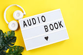 inscription audiobook on a light box with modern white headphones on a yellow background