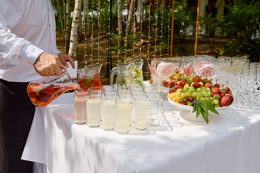 The barman pouring drink into the glass outdoors. Bartender pouring juice from a pitcher at wedding reception. The concept of service.