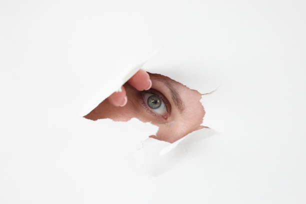 istock Female eye looks through hole in white paper 1311273952
