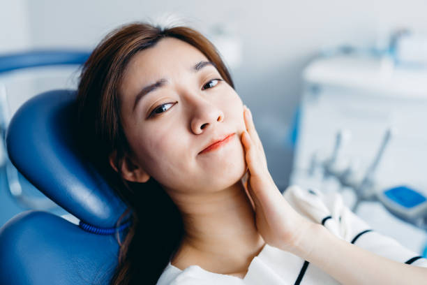 アジアの若い女性は痛みを感じ、歯科医院で頬を手で握っている。歯痛の概念。 - ヒトのアゴの骨 ストックフォトと画像