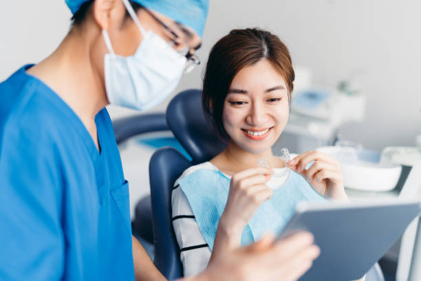 asiatischer zahnarzt erklärt zahn-röntgen strahlen einem patienten mit digitalem tablet. asiatische junge attraktive frau mit kieferorthopädischen retainern in der zahnklinik. invisalign kieferorthopädie konzept. - zahnschiene stock-fotos und bilder