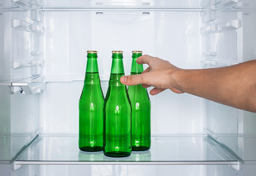 Man's hand reaches for a bottle of beer in the fridge. Alcoholism.