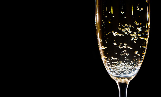 Champagne with bubbles in a glass on a black background. Copy space, macro.