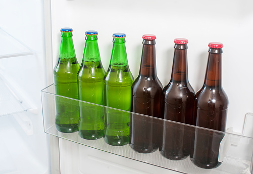 Many green and brown glass beer bottles stand on the fridge door.
