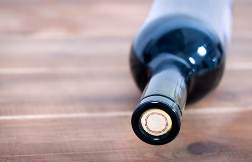 A closed bottle of wine with a cork lies on a wooden table close-up, macro.
