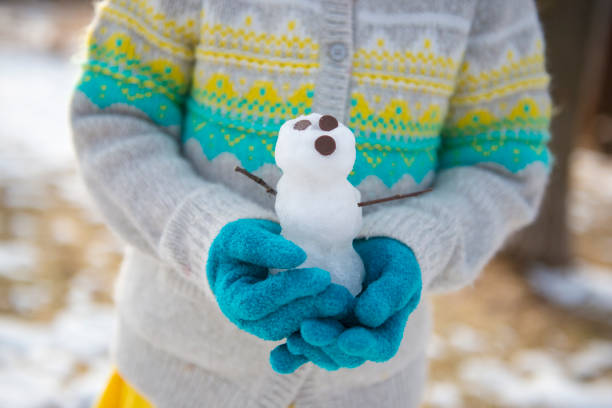 istock Child outdoors with blue gloves holding tiny snowman. 1311293213