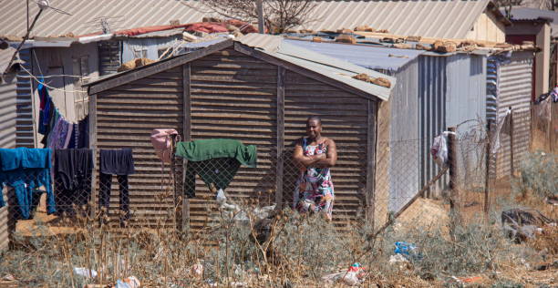 afrikanische frau, die vor ihrem haus steht und darauf wartet, dass die kleidung in einem einkommensviertel von soweto trocken wird. - rusty city life metal rust stock-fotos und bilder