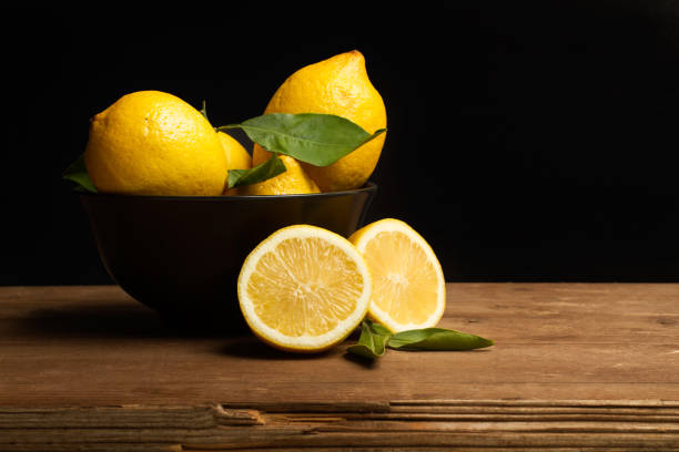 Lemons in a black bowl and on a wooden table