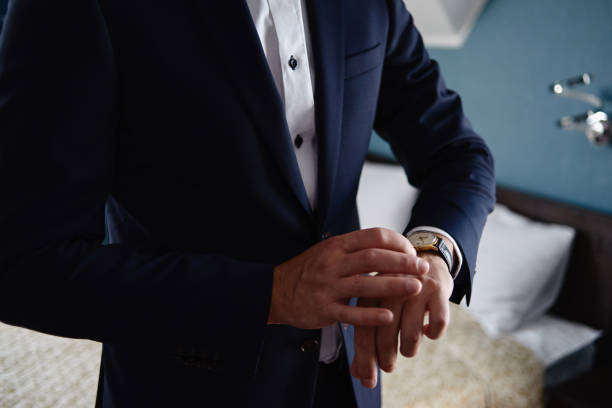 Businessman looking at watches on his hand indoors, copy space. Man in blue suit checking time from luxury wristwatches. Watch on hand. Groom wedding preparation stock photo