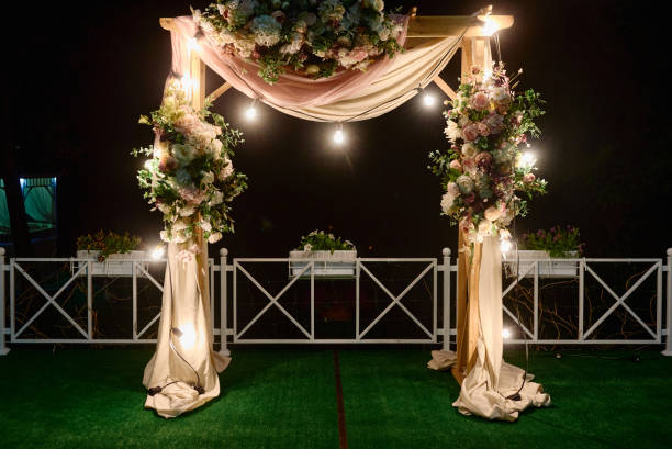 istock Night wedding ceremony with arch, flowers, cloth and bulb lights on the backyard outdoors, copy space. Wedding decor 1311296174