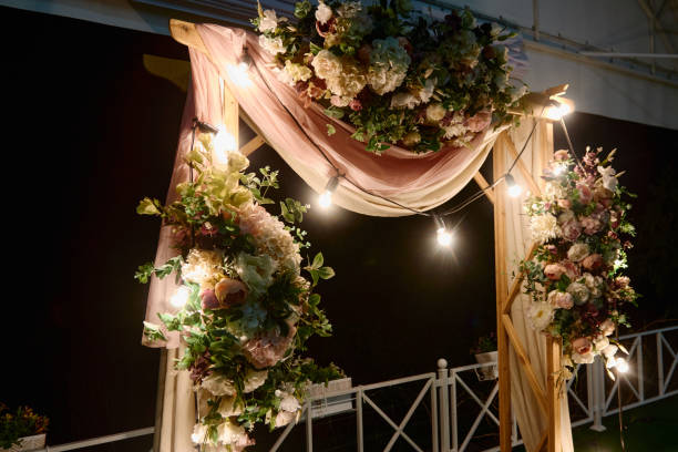 istock Night wedding ceremony with arch, flowers, cloth and bulb lights on the backyard outdoors, copy space. Wedding decor 1311296175