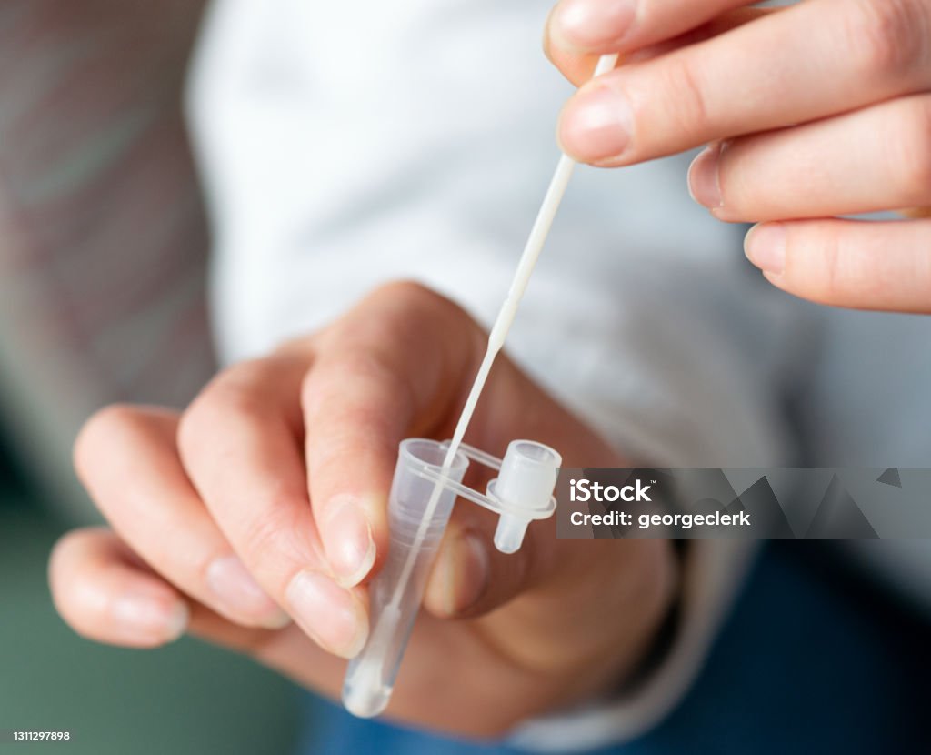 Home testing for Coronavirus - lateral flow test swab Close-up as a woman follows the steps for a lateral flow test at home, putting the swab into the buffer solution in a plastic vial. Cotton Swab Stock Photo