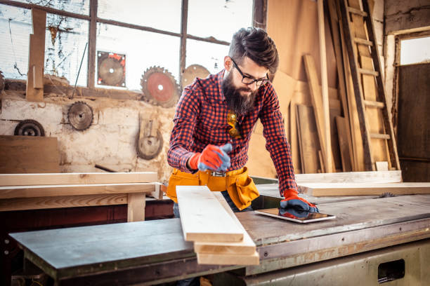 istock Young man at carpentry cutting wood with a circular saw and using digital tablet. 1311297958