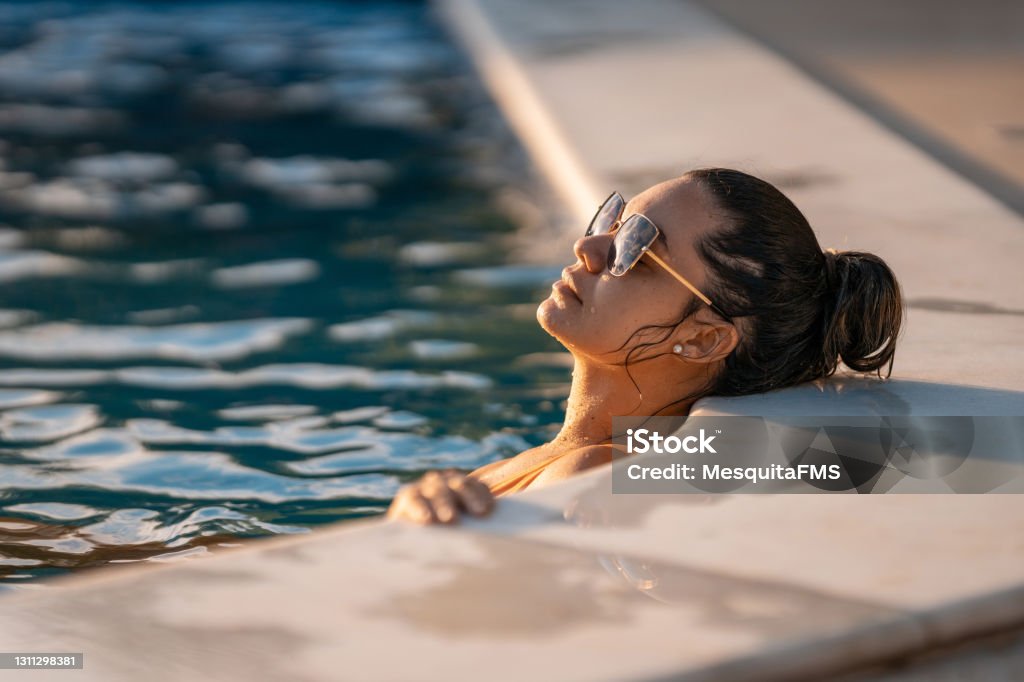 Young woman sunbathing in the pool Young woman sunbathing in the pool at sunset Swimming Pool Stock Photo