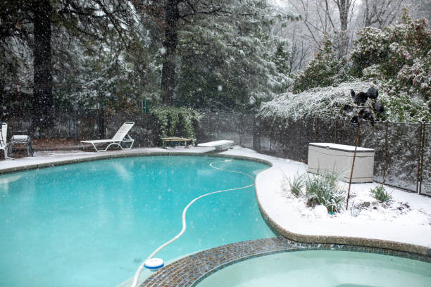 piscine d’hiver d’arrière-cour dans la neige avec l’eau bleue claire et les arbres blancs - winterizing photos et images de collection