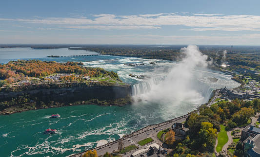 Aerial view of Horseshoe Falls and nearby island on Niagara river with a tall cloud of water drops in a sunny autumn day