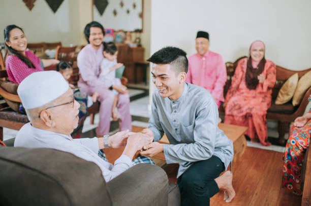 neto muçulmano malaio em roupas tradicionais mostrando gesto de desculpas para seu avô haji durante a celebração aidilfitri família malaia em casa celebrando hari raya - great granddaughter - fotografias e filmes do acervo