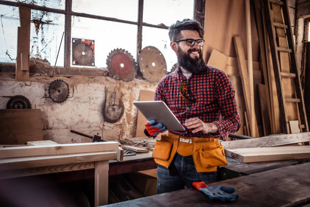 istock Young man at carpentry cutting wood with a circular saw and using digital tablet. 1311302032