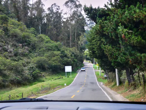 Single uneven road with one car between the trees and the hills.