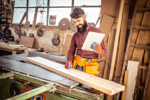 istock Young man at carpentry cutting wood with a circular saw and using digital tablet. 1311308126