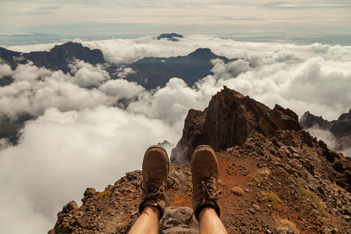 Subjective point of view shot of the landscape and hiking boots of a man, sitting on the top of the Roque de los Muchachos viewpoint, on the island of La Palma, Canary Islands, Spain.