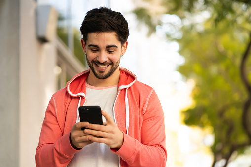 Portrait of young man using his mobile phone while walking outdoors on the street. Urban concept.