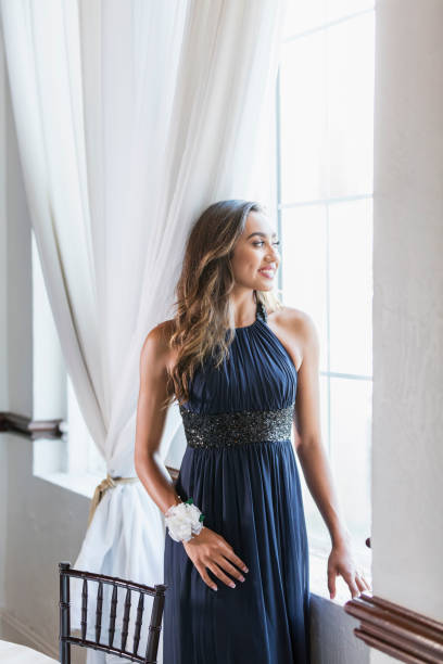 Mixed race teenage girl wearing prom dress A mixed race teenage girl, 16 years old, standing by a window, wearing a prom dress and wrist corsage. prom dress stock pictures, royalty-free photos & images