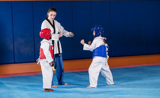A taekwondo instructor standing between two 7 year old boys wearing protective vests and helmets, ready for a competition or to practice their skills.