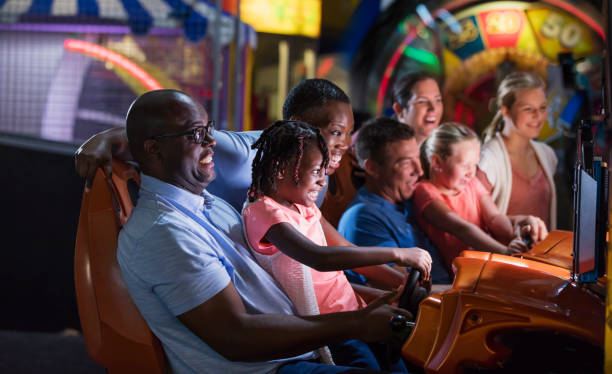 Two families playing an arcade game Multi-ethnic group of friends and family, seven people, having fun at an amusement arcade. The two families are playing an auto racing video game. The main focus is on the African-American family with their 7 year old daughter. arcade photos stock pictures, royalty-free photos & images