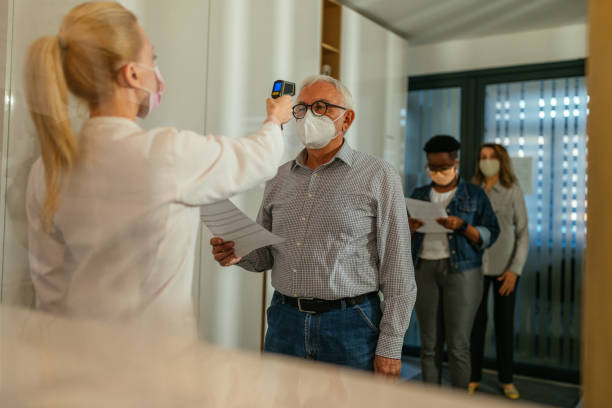 doctor in face mask using non-contact thermometer to measure patients body before vaccination - infrared thermometer imagens e fotografias de stock