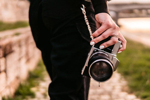 Woman holding retro camera in hand outdoors, close up.