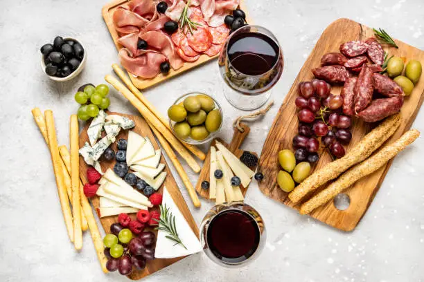 charcuterie board with pork sausage, salami and cheese plate with brie, parmesan pecorino and gorgonzola. served with grapes. olives and blueberries with grissini breadsticks. food flat lay