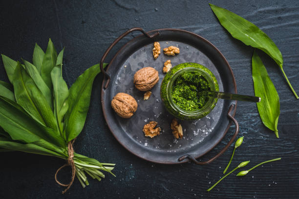 Homemade wild garlic pesto and walnuts on a metal tray, wild garlic leaves and blossoms on black background Homemade wild garlic pesto and walnuts on a metal tray, wild garlic leaves and blossoms on black background ramson stock pictures, royalty-free photos & images