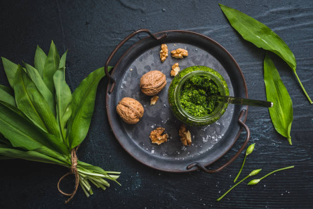 pesto de alho selvagem caseiro e nozes em uma bandeja de metal, folhas de alho selvagem e flores no fundo preto - ramson - fotografias e filmes do acervo