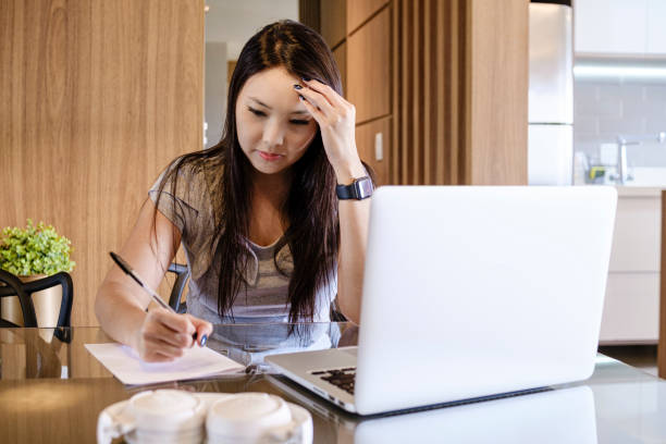 istock Young Asian woman touching her forehead trying to concentrate while writing 1311328065