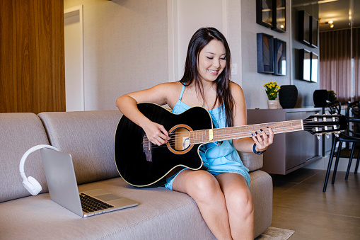 Asian woman creating musical improvisation with guitar.