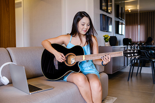 Portrait of asian woman enjoying a relaxing moment at home playing the guitar..
