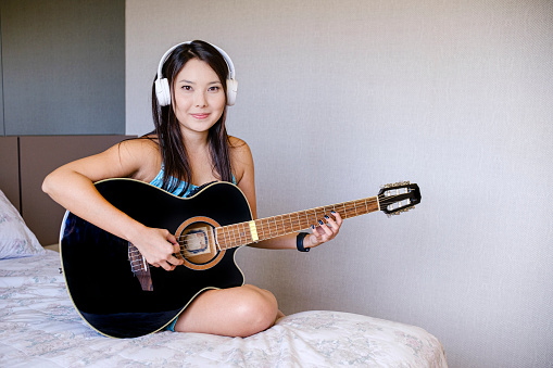 Asian young woman playing guitar in his room.