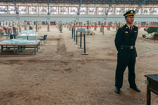 Xian, China - May 1, 2010: Terracotta Army of Qin Shi Huang. Security guards in hall over beige dirt excavations with hundreds of soldier and horse statues.