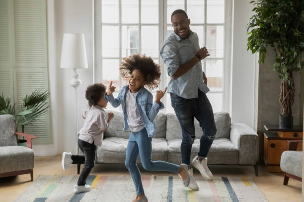 Cool daddy entertaining two children at home Cool daddy entertaining two children at home. Funny black dad or babysitter and excited active kids dancing, running rounds in living room, laughing, having fun, going crazy. Family activity concept dancing dad stock pictures, royalty-free photos & images