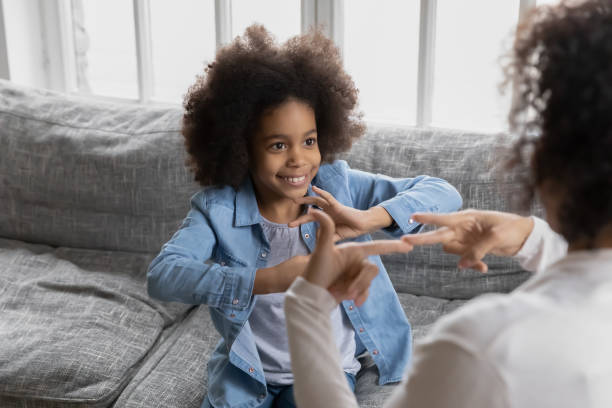 Happy Black girl talking to disabled deaf mom Happy girl talks to disabled deaf mom. Mother teaches kid sign language, shows hand gestures and finger symbols. Tutor giving lesson to positive child with hearing disability at home. Children therapy deafness photos stock pictures, royalty-free photos & images