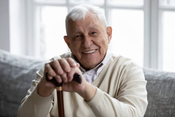 feliz abuelo mayor sentado en el sofá sonriendo demostrando dientes sanos - one senior man only grandfather portrait old fotografías e imágenes de stock
