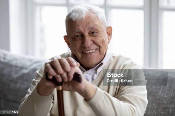 Happy Senior Grandfather Sitting On Couch Smiling Demonstrating Healthy Teeth Stock Photo - Download Image Now