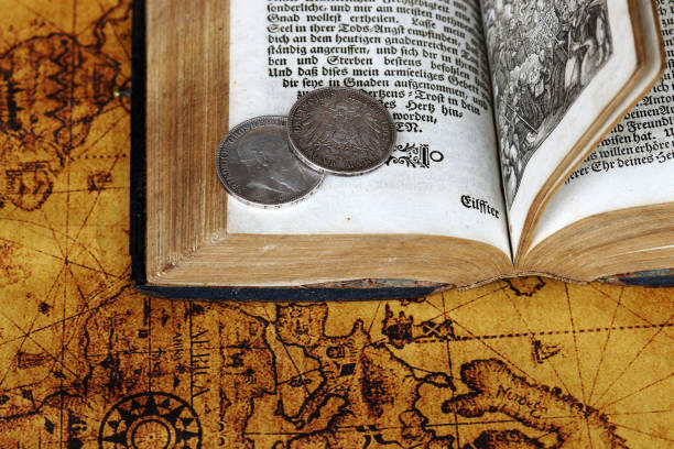 Old silver coins from 1902 and an antique book from 1763 on a world map
